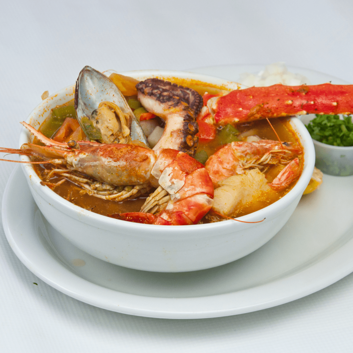 A plate with a bowl of meat in a sauce and fresh veggies and limes